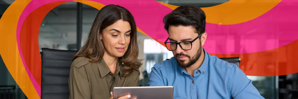 Two people sit at a table in an office, looking at a tablet together with colorful orange and pink wave graphics in the background.