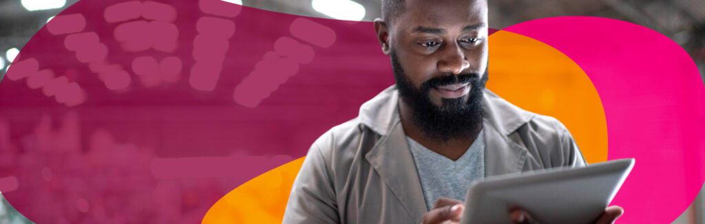 Man in a coat uses a tablet against a blurred abstract background with pink and orange shapes.