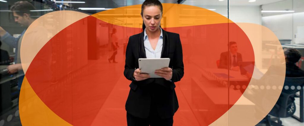 A person in a dark suit is standing indoors holding a tablet. The background includes people working and red and orange abstract shapes overlay the image.