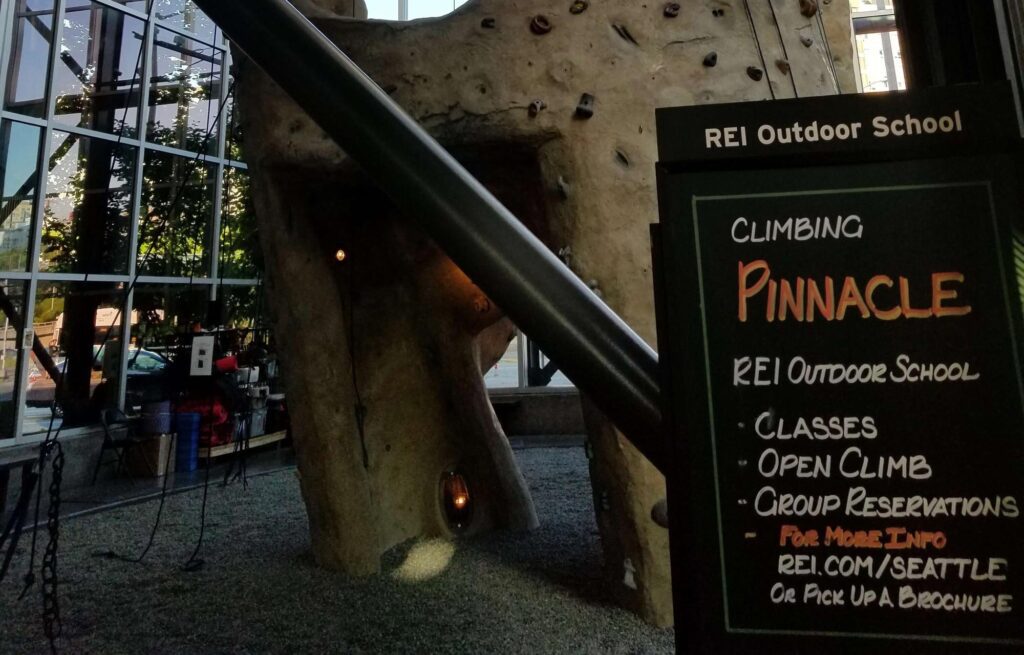 Indoor climbing wall with a sign advertising REI Outdoor School classes and reservations.