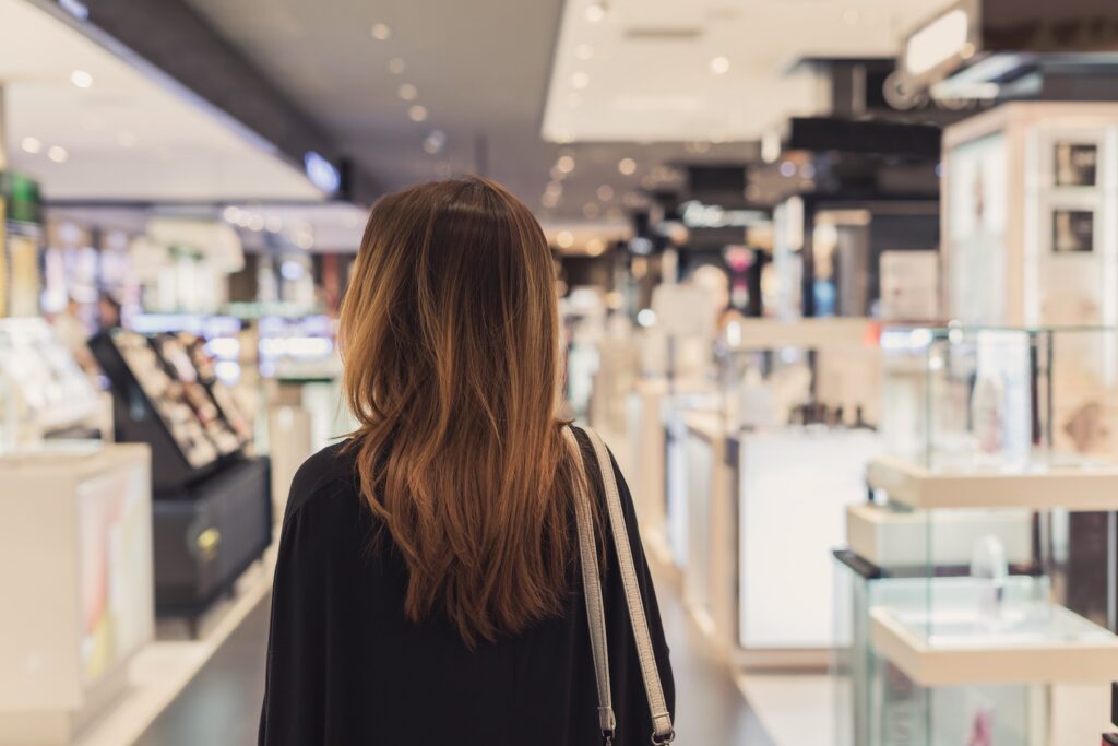 Person with long brown hair browsing in a brightly lit store with shelves of products.