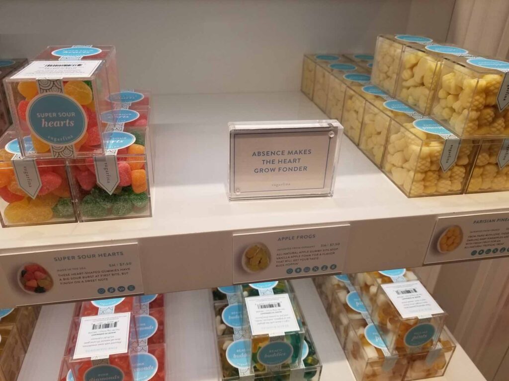 Shelves displaying various boxed candies, including colorful sour hearts, apple frogs, and pear-inspired treats, with a sign stating "Absence makes the heart grow fonder.