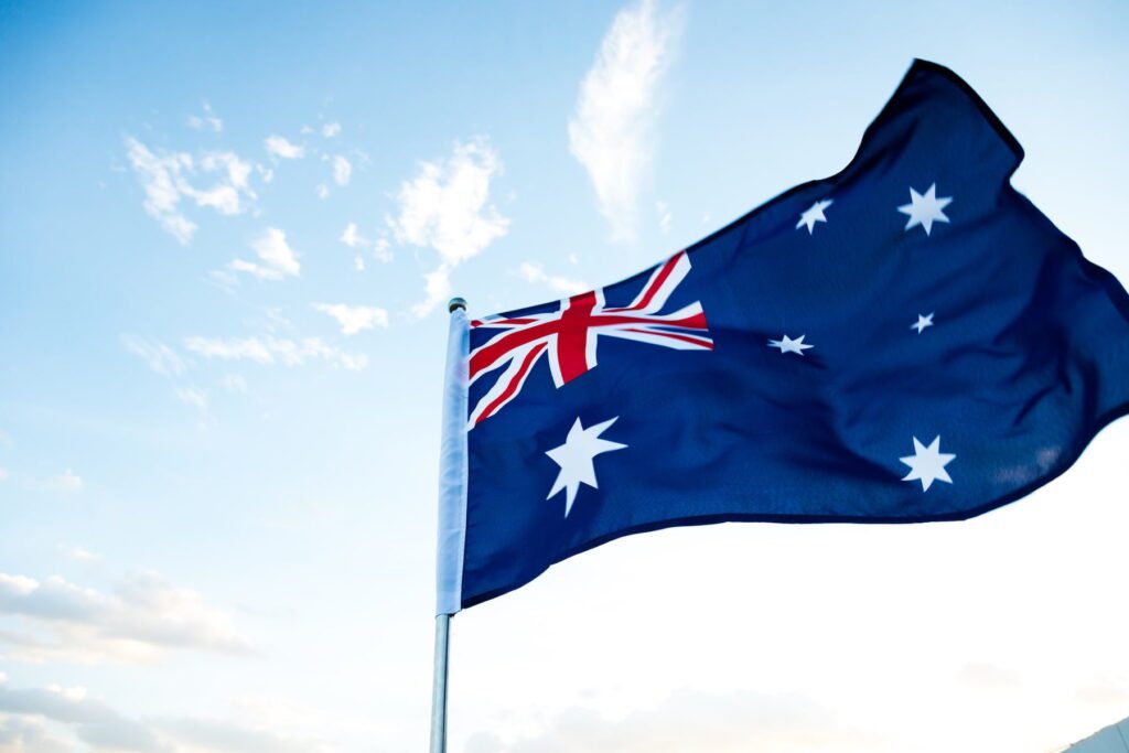 The Australian flag waves against a clear blue sky with some clouds.