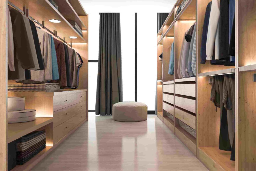 A modern walk-in closet with wooden shelves, hanging clothes, folded items, drawers, and a round ottoman by a tall window with dark curtains.