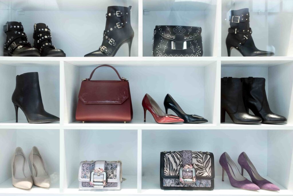 A collection of women’s heeled shoes, ankle boots, and handbags displayed on white shelves.