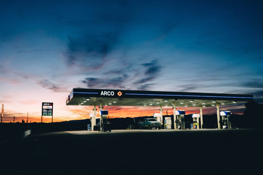 A brightly lit ARCO gas station at dusk with several fuel pumps and a car, set against a colorful sunset sky.