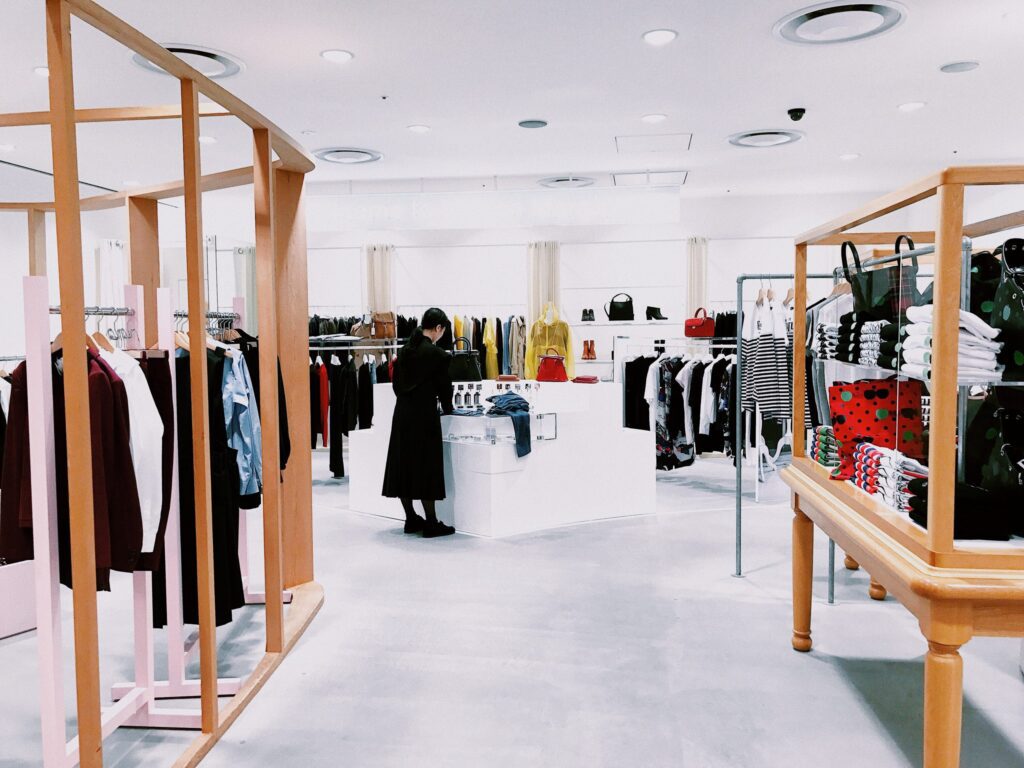 A woman browses clothing racks in a brightly lit, modern retail store displaying various garments and accessories.