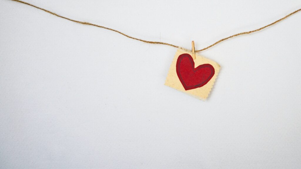 A piece of twine is stretched across a white background with a clothespin holding a square card featuring a red heart.