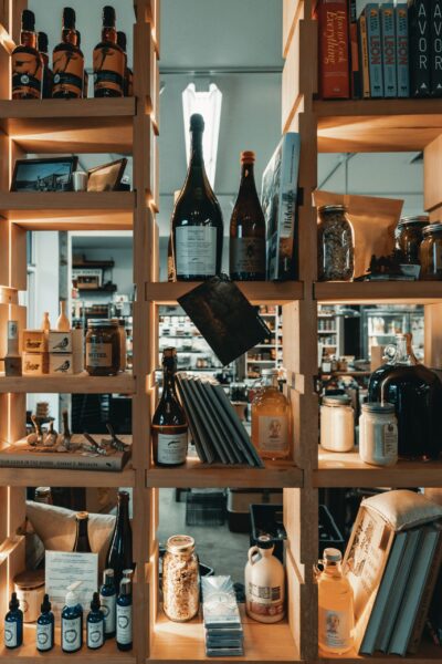 Wooden shelves display bottles, jars, books, and various packaged goods in a well-lit store or shop interior.