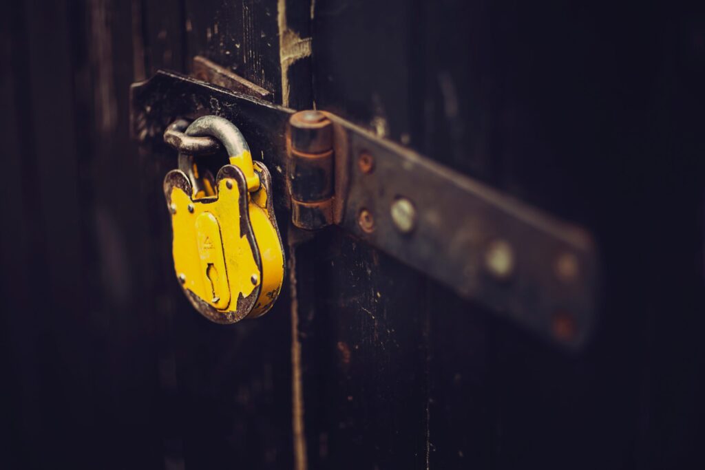 A close-up of a weathered black metal gate secured with a large, yellow padlock.