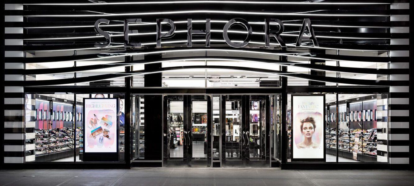 A Sephora store entrance with large glass doors flanked by display windows showcasing beauty products and promotional posters.