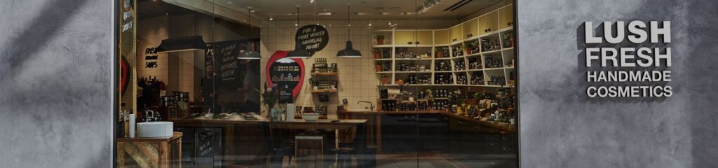 Storefront of Lush Fresh Handmade Cosmetics with a glass display showing shelves of products inside.