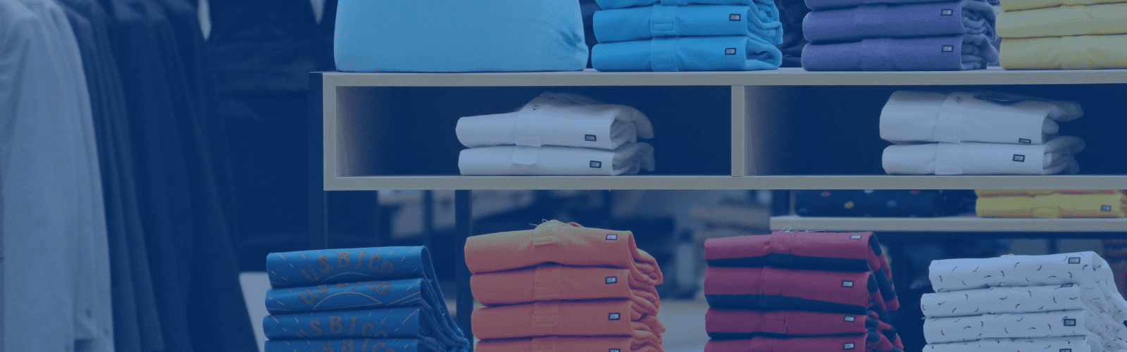 Stacks of neatly folded shirts in various colors are displayed on shelves in a clothing store.