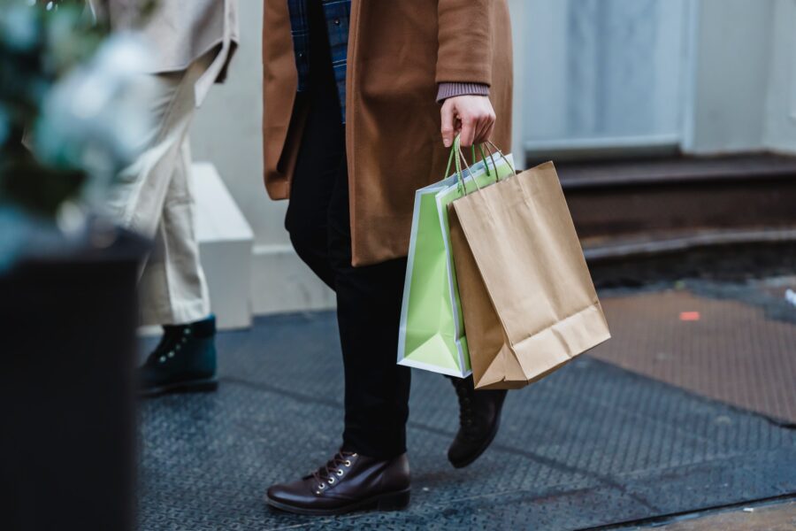 Person walking while carrying two shopping bags, one brown and one green, on a city street.
