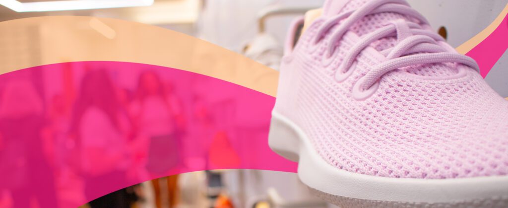 Close-up of a pink athletic shoe with a pink and orange abstract overlay. Blurred figures are visible in the background.