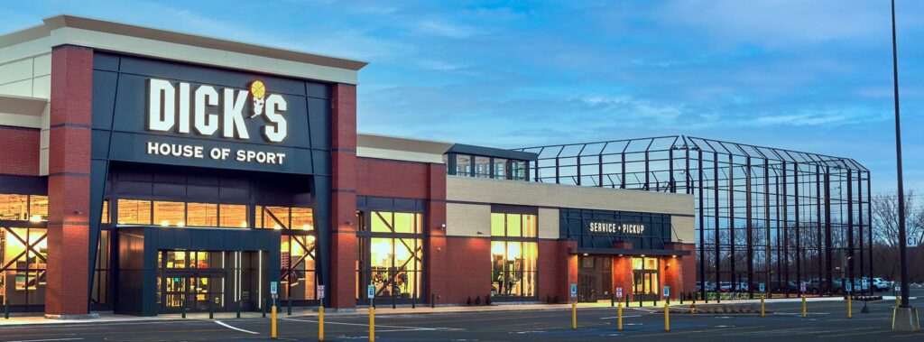 Exterior view of a Dick's House of Sport store with large windows and parking lot under a cloudy sky.