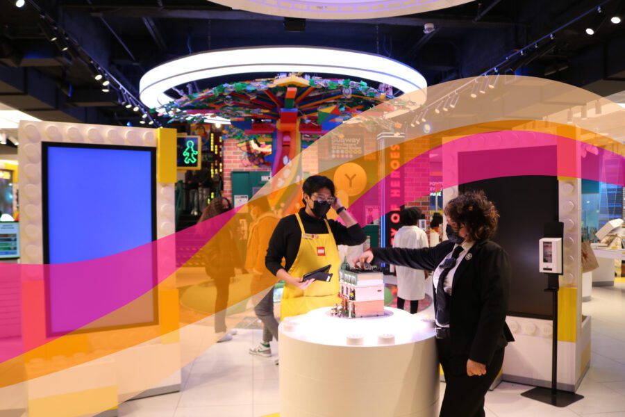 Store employees interacting at a display counter inside a brightly lit store with colorful decorations and digital screens.