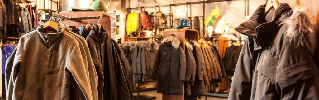 A clothing store with various jackets and coats hanging on racks, featuring different styles and colors, including ones with fur trim.