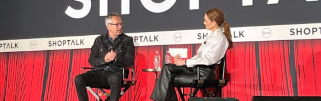 Two people are seated on a stage at a ShopTalk event, engaged in conversation. The backdrop features the word "ShopTalk" repeatedly.