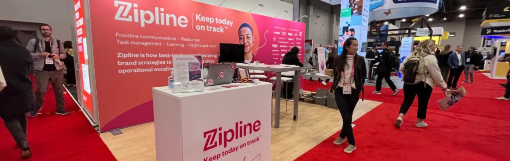 Trade show booth for Zipline featuring promotional material, a table with devices, and attendees walking by on a red carpet.