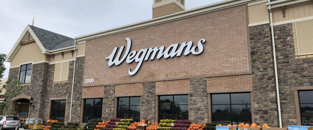Front view of a Wegmans grocery store with pumpkins and flowers displayed outside.