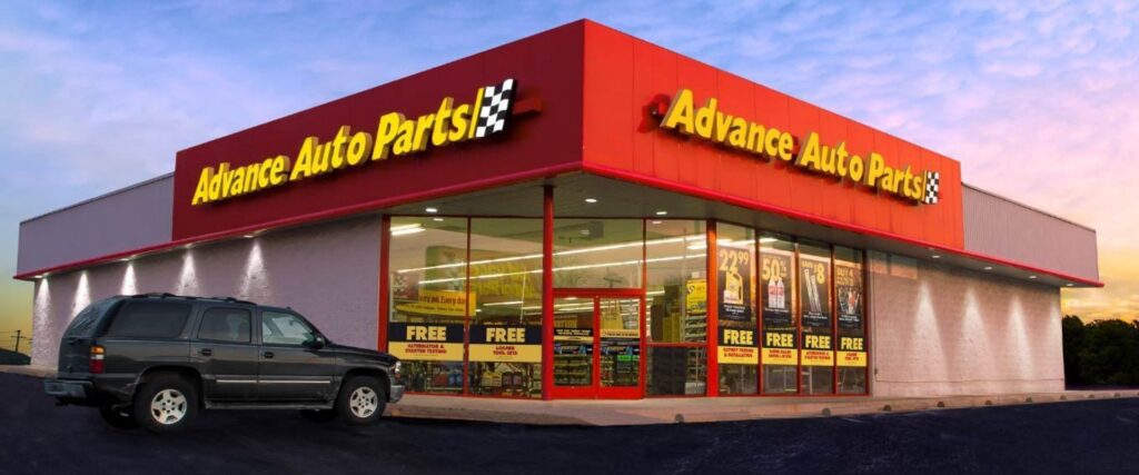 Exterior view of an Advance Auto Parts store with a black SUV parked in front. The store's windows display promotional signs.