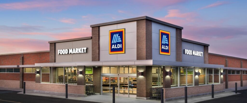 Exterior of an Aldi Food Market store at sunset, featuring the store's signage and glass entrance.