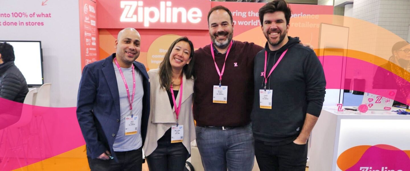 Four people smiling and standing together in front of a Zipline booth at an event, wearing name badges and pink lanyards.