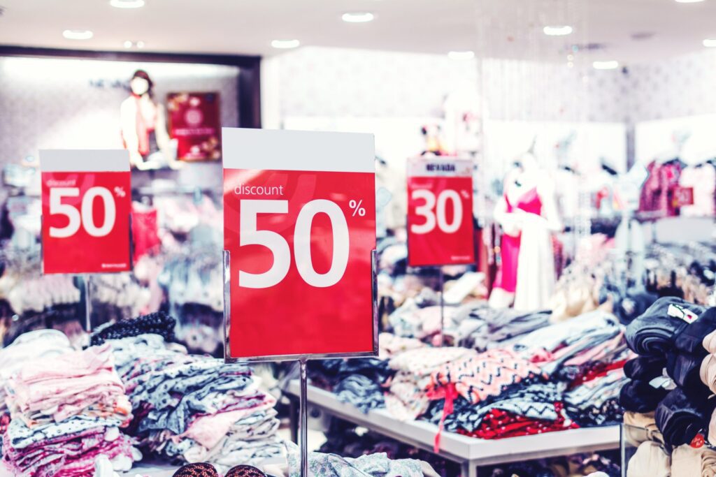 Clothing store interior with prominently displayed red signs advertising a 50% discount; racks of folded clothes are visible in the background.