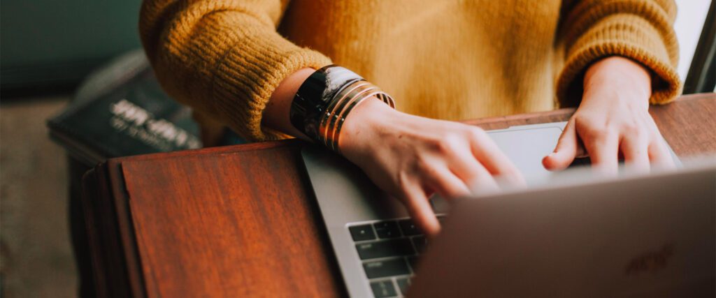 Person typing on a laptop, wearing a yellow sweater and multiple bracelets.