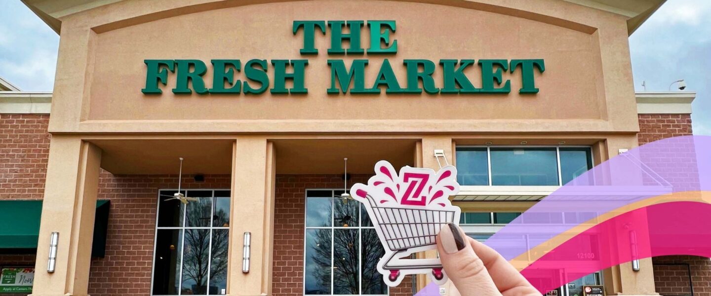 Person holding a shopping cart sticker in front of The Fresh Market store entrance.