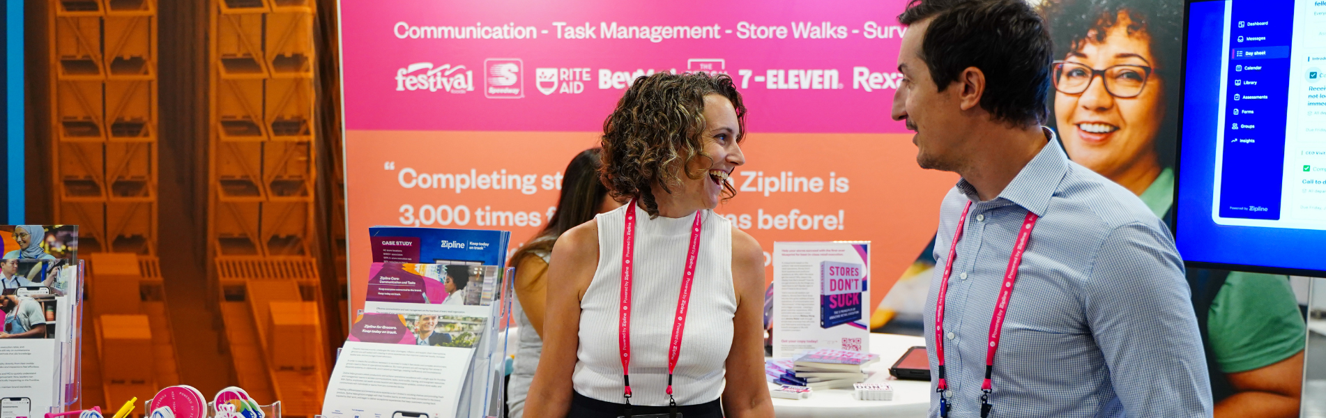 Two people standing and smiling at an event booth promoting business communication and task management solutions, with various promotional materials displayed.