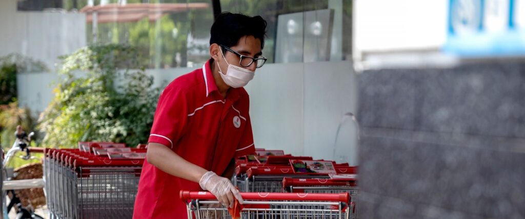 Person in a red shirt and mask pushes shopping carts outdoors.