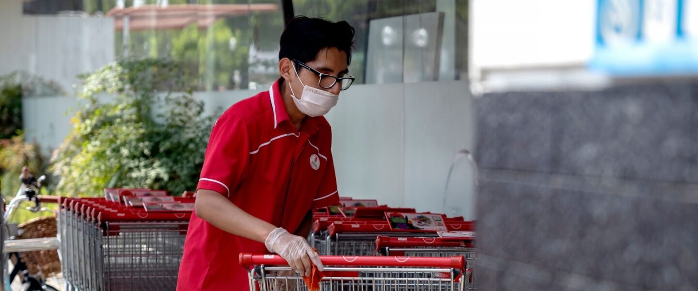 Person in a red shirt and mask pushes shopping carts outdoors.