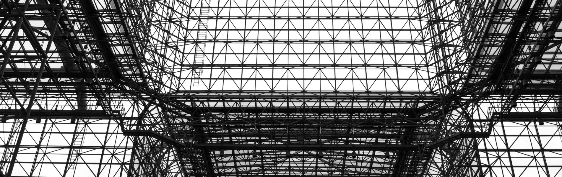 Black and white image of a complex glass and steel structure with crisscrossing beams forming a geometric pattern.