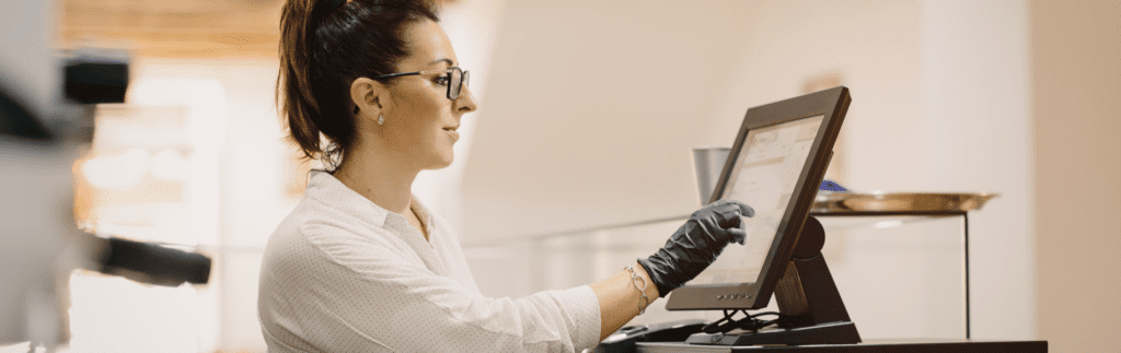 Woman using a touchscreen at a counter, wearing glasses and a glove.