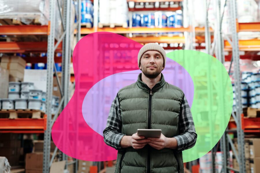 A man in a beanie and vest holds a tablet in a warehouse with shelves stacked with cans and boxes. Colorful abstract shapes are overlaid.