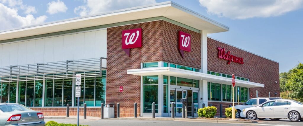 Exterior of a Walgreens pharmacy building with red signage, large windows, and parked cars in the foreground.
