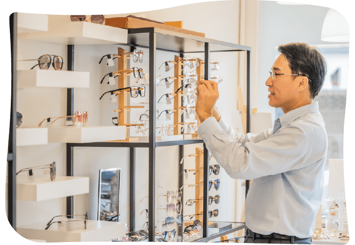 A man examines a pair of glasses on a display rack in an eyewear store.