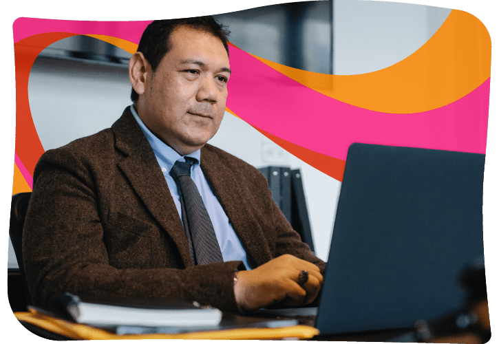A man in a suit jacket and tie works on a laptop at a desk, with a notebook and pen nearby. A colorful abstract design is in the background.