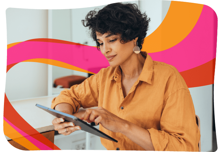 A person in an orange shirt uses a tablet at a desk, with abstract pink, orange, and yellow wave graphics in the background.