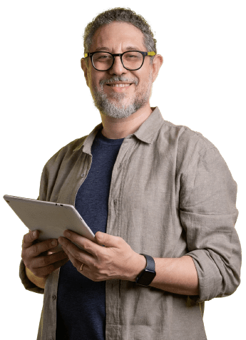 A smiling man with glasses holds a tablet. He is wearing a beige shirt over a dark T-shirt and has a watch on his left wrist.