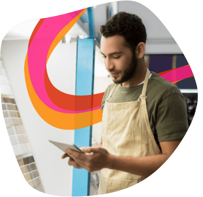 A person wearing an apron is using a tablet in a store, standing near a display with colorful ribbons.