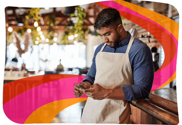 Man in apron standing by a counter, looking at a smartphone, with colorful swirls in the background.