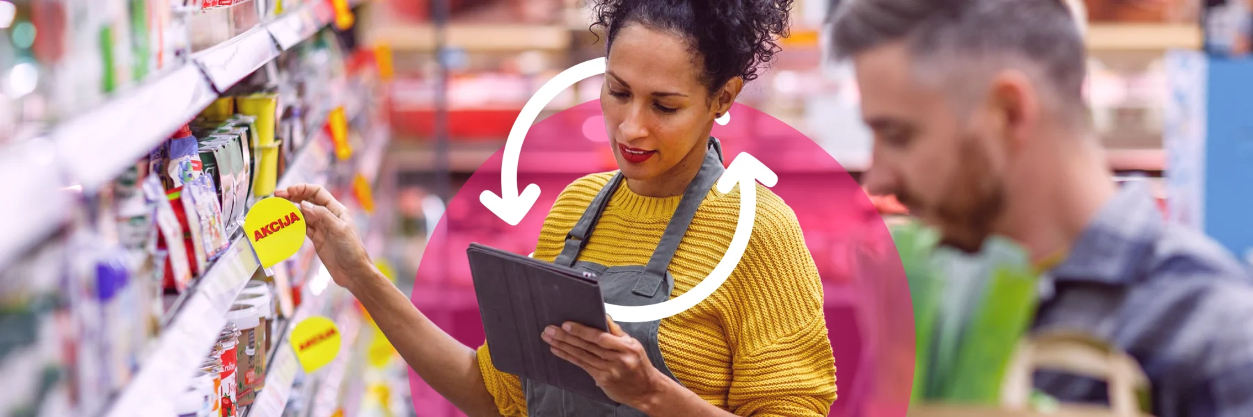 Woman in a yellow sweater checks a tablet while standing in a store aisle, as a man shops nearby. Shelves are stocked with various products.