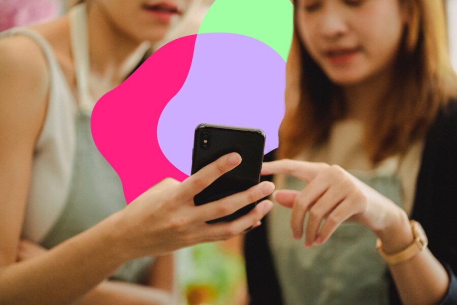 Two people focus on a smartphone, one holding the device while the other points at the screen. Bright abstract shapes are overlaid in the background.