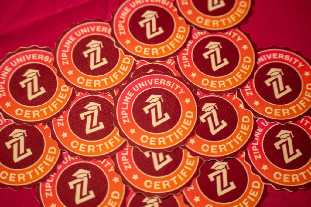 A pile of red and orange circular stickers labeled "Zipline University Certified" with a graduation cap and a "Z" in the center.