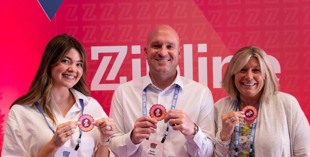 Three people stand in front of a red Zipline backdrop, smiling and holding up round Zipline-branded stickers or badges.