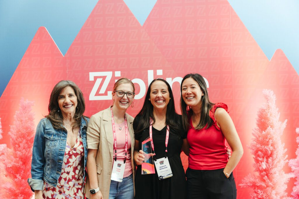 Four women stand smiling in front of a red geometric Zipline backdrop; one woman holds an award.