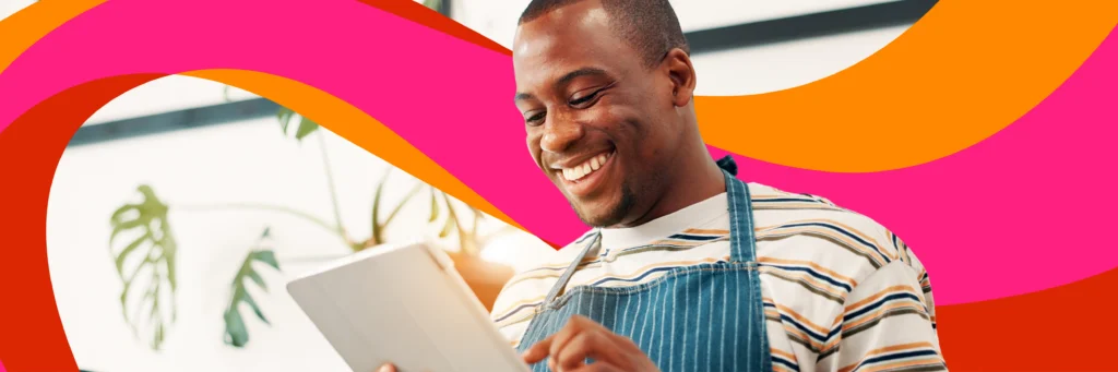 A man wearing a striped shirt and apron smiles while using a tablet, with colorful pink and orange graphic shapes in the background.